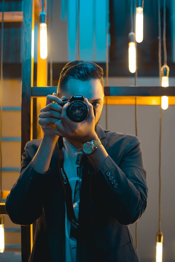 A stylish photographer in a modern setting capturing a shot with ambient lighting.